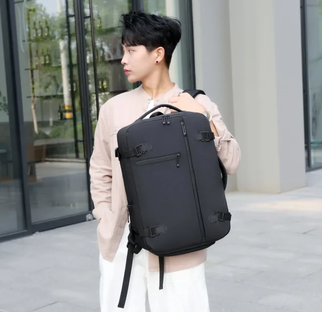 A person holding a black KB3726 backpack with a front zip pocket and compression straps
